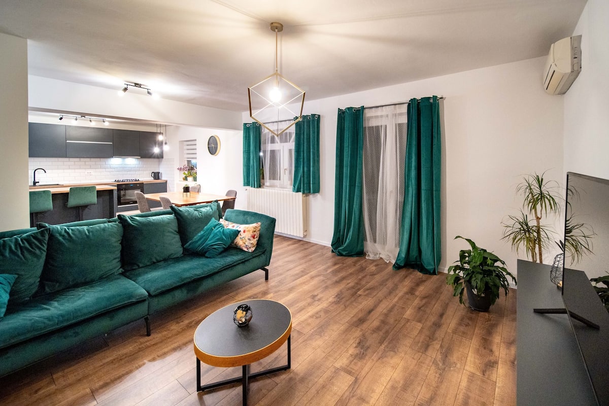A modern living room with a green sofa, a coffee table, and a kitchen in the background.