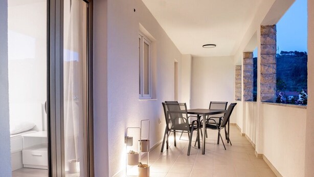 A balcony with a table and chairs, a lit candle, and a view of the sea. - Apartment Grguric Apartments (Rab)