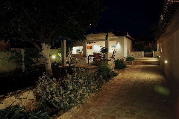 A well-lit outdoor patio area with a dining table and chairs, surrounded by stone walls and plants. - House Mrcela 200m From Beach (Okrug)