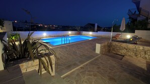 A rectangular swimming pool with a stone deck, surrounded by potted plants and a stone wall. - House Mrcela 200m From Beach (Okrug)