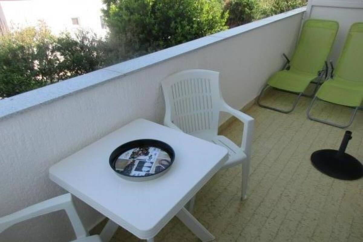 Een klein balkon buiten, met een witte tafel en twee groene stoelen.