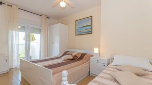 Een slaapkamer met een bed, nachtkastjes, een ventilator in het plafond, een schilderij en uitzicht door een raam.