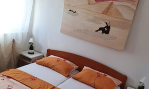 A bedroom with a bed, a nightstand, a lamp, and a painting on the wall. - Apartment Olive Shared Pool (Pirovac)