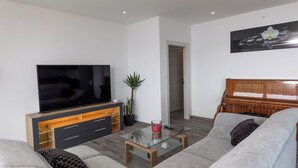 A modern living room with a flat-screen TV, a glass coffee table, a sofa, a wooden cabinet, and a potted plant. - Apartment Ida (Crikvenica)