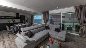 A modern living room with a grey sectional sofa, a glass dining table, and a view of the sea. - Apartment Ida (Crikvenica)