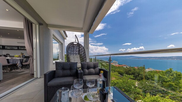 A balcony with a dining table set for four, a wicker sofa, and a view of the sea. - Apartment Ida (Crikvenica)
