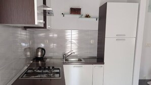 A modern kitchen with a gas stove, sink, and white cabinets. - Apartments Dariana (Makarska)