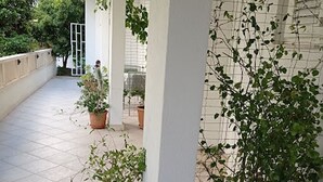 A covered outdoor area with tiled flooring, white pillars, and potted plants. - Apartments Dariana (Makarska)