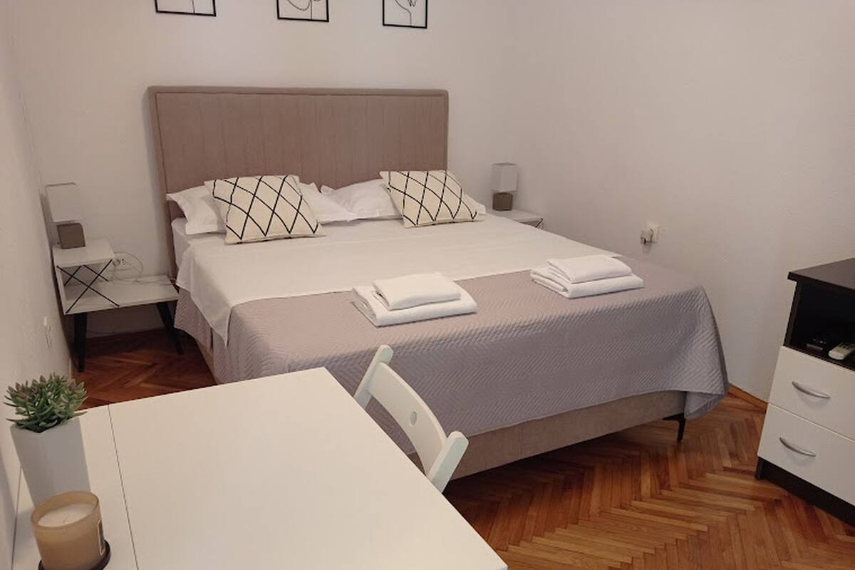 A neatly arranged bedroom with a bed, bedside tables, a small table, and a chair.