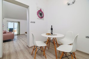 Un'area pranzo con un tavolo rotondo, quattro sedie bianche, una bottiglia di vino e un orologio appeso al muro.