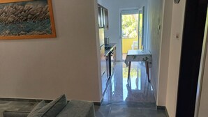 A hallway with a sofa, a painting, and a kitchen area with a table and chairs. - Apartment Maris (Karlobag)