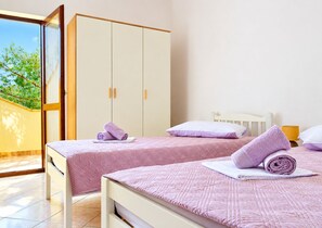 A bedroom with two beds, a wardrobe, and a view of greenery outside. - Apartment Maris (Karlobag)