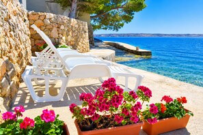 A seaside terrace with white lounge chairs, a stone wall, and a view of the sea. - Apartment Maris (Karlobag)