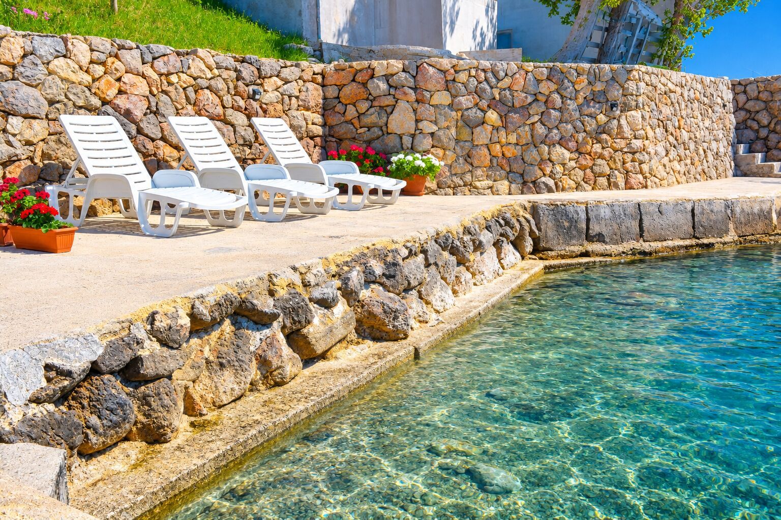 Ein Poolbereich mit Steinmauern, klarem Wasser und Liegestühlen.