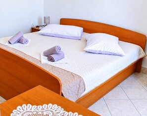 Ein ordentlich bezogenes Bett mit Holz-Kopfstück, zwei Kissen und zwei aufgerollten Handtüchern.