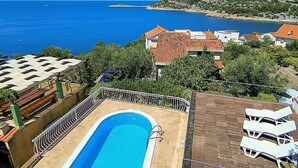 A pool with a view of the sea, a building with a tiled roof, and a hillside. - House Villa Carmen (Rogoznica)