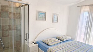 A bedroom with a shower, a bed with striped bedding, and two framed pictures on the wall. - House Villa Carmen (Rogoznica)