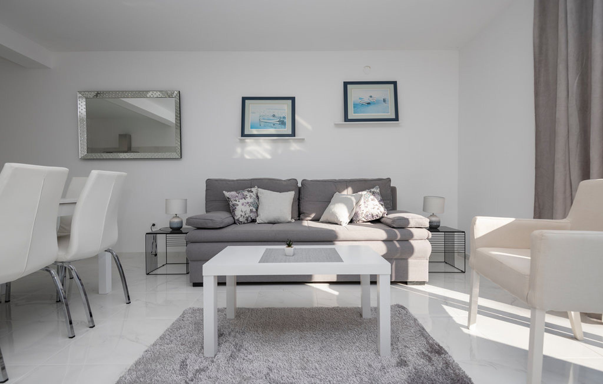 Una sala de estar moderna con un sofá gris, una mesa de centro blanca y dos cuadros enmarcados en la pared.