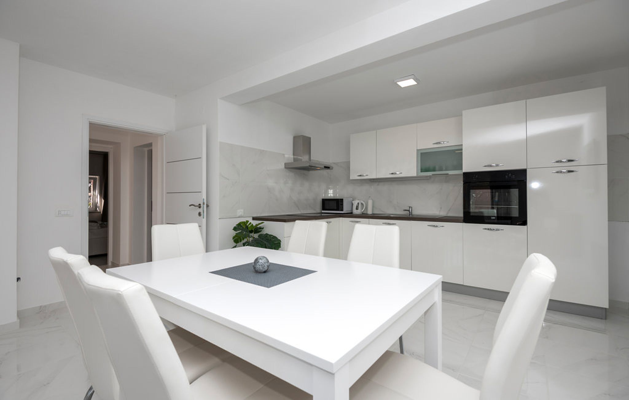 Een moderne keuken met witte kasten, een eettafel met stoelen en een magnetron.