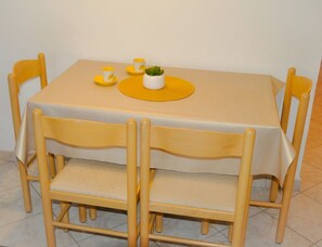 Ett matbord med en gul duk, sex trästolar och en liten krukväxt på bordet.