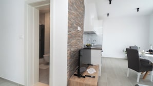 A modern kitchen with a brick accent wall, a dining area with a table and chairs, and a visible bathroom. - Apartments Kate (Rogoznica)