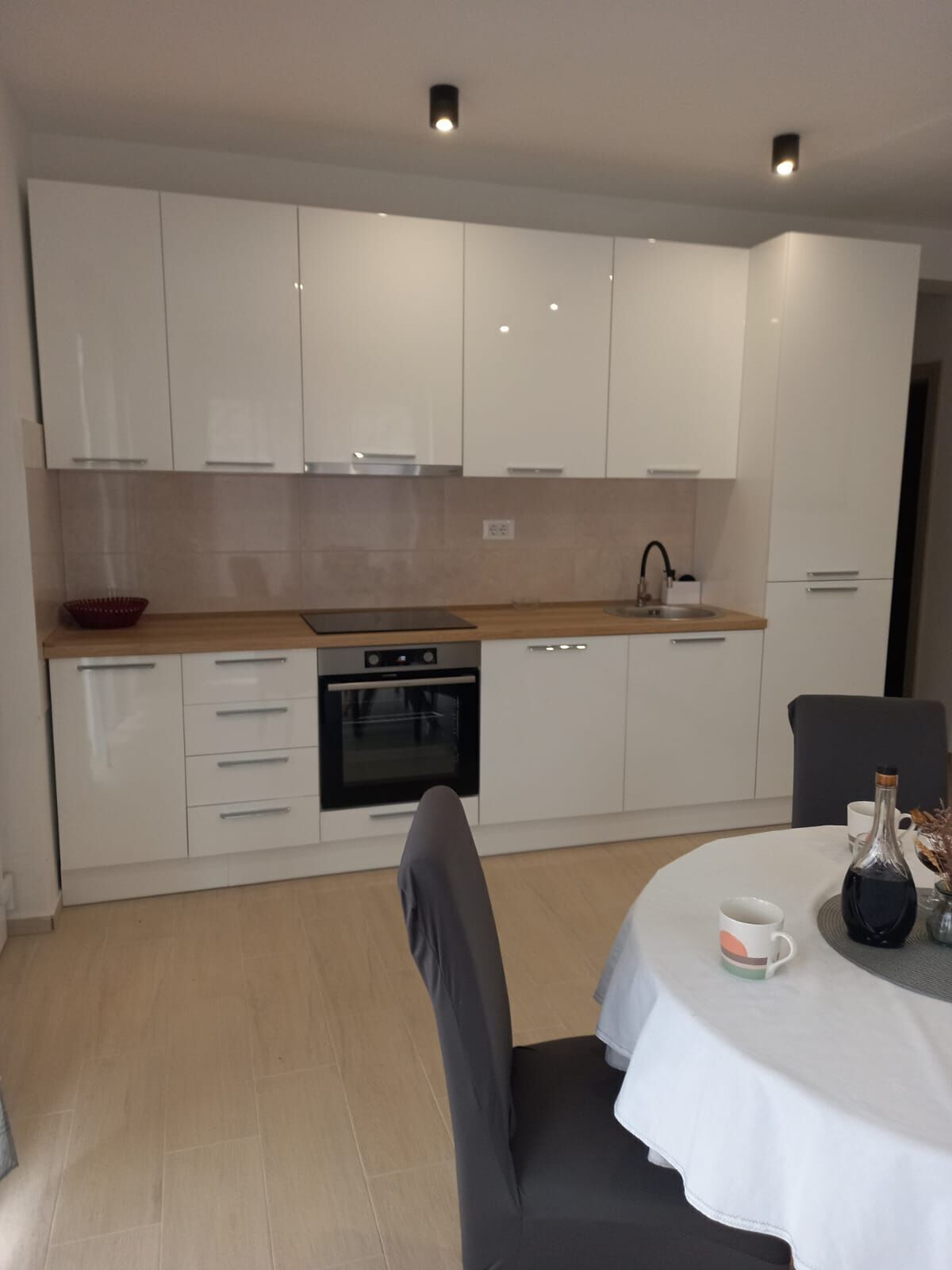 A modern kitchen with white cabinets, a wooden countertop, an oven, and a dining area with a table and chairs.