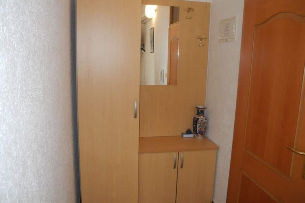 A wooden wardrobe with a mirror above a shelf, a small vase, and a door with a brass handle.