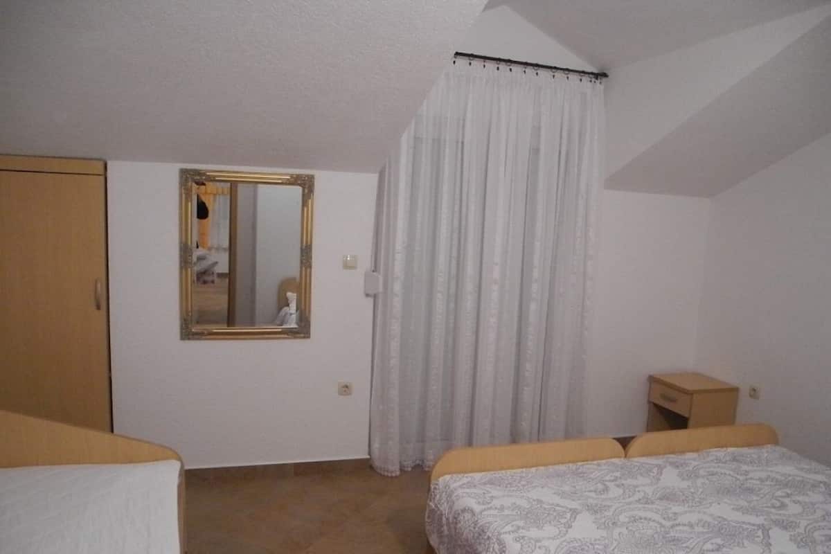 A bedroom with a bed, a wardrobe, a mirror, and a window with curtains.