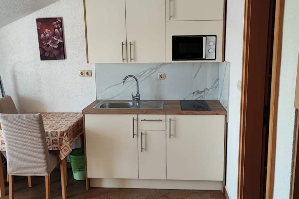 A compact kitchen with a sink, microwave, and cabinets. There is a dining table with chairs and a small sofa.