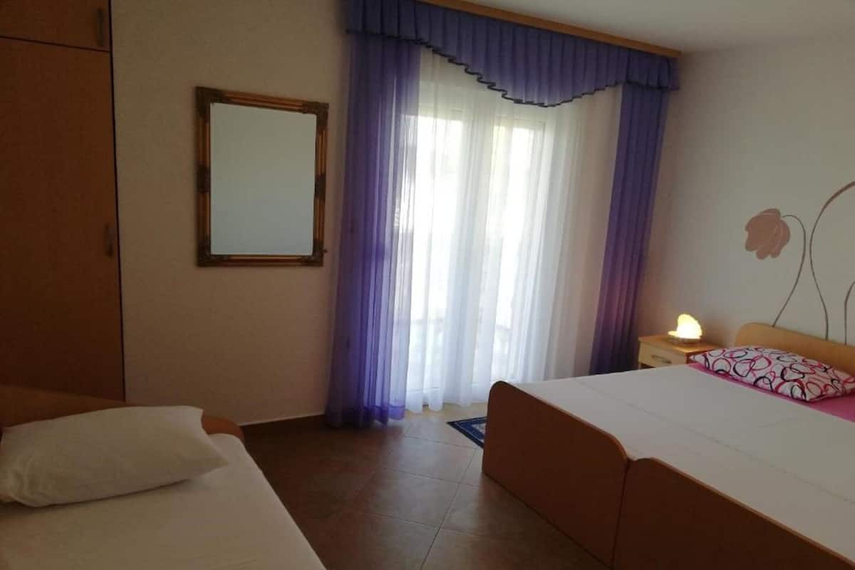 A hotel room with a bed, a nightstand, a mirror, and a window with purple curtains.
