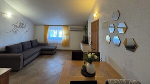 A living room with a sectional sofa, a dining table with a vase of flowers, and a wall with hexagonal mirrors. - Apartments Maca (Sibenik)
