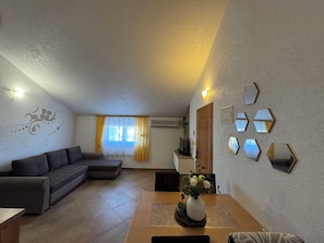 En stue med en hjørnesofa, et spisebord med en vase blomster, og en væg med sekskantede spejle.