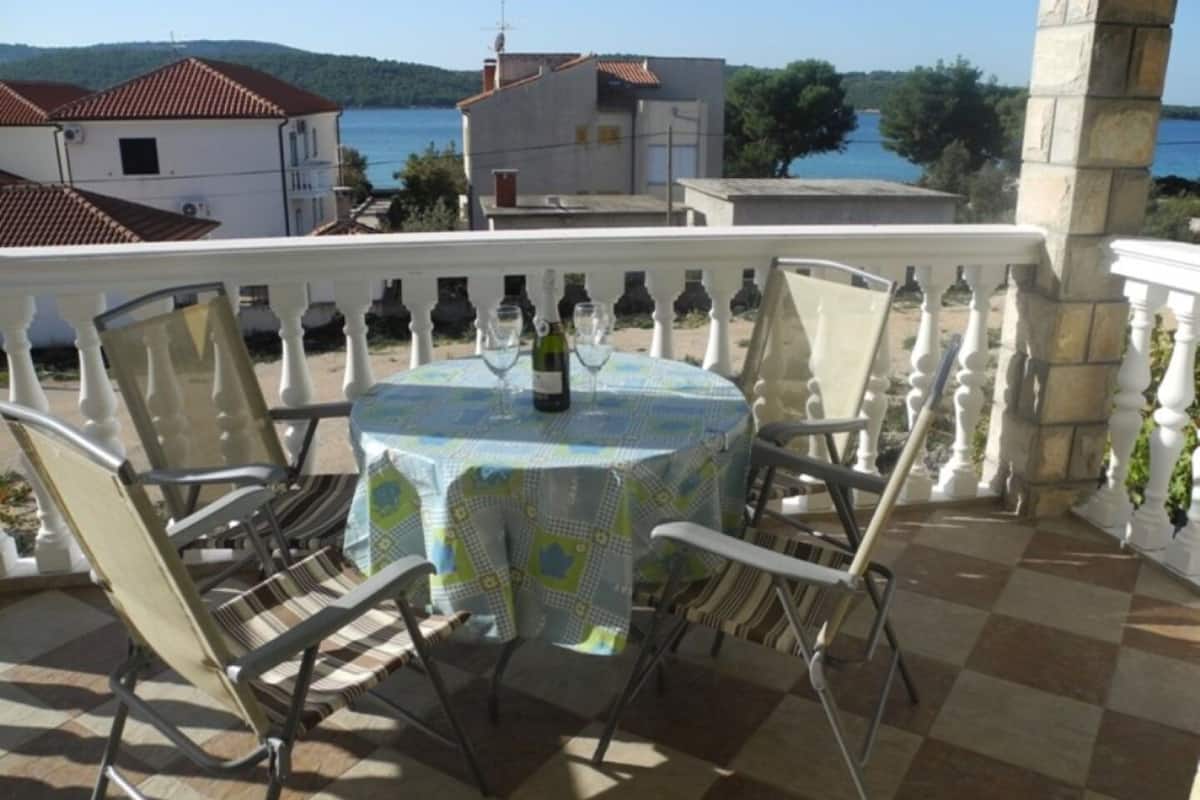 A terrace with a round table, chairs, and a view of the sea and buildings.