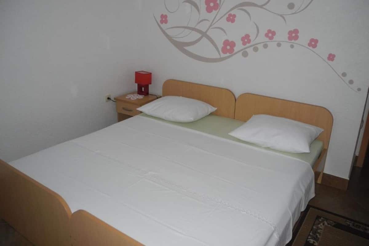 A bedroom with a bed, two pillows, a nightstand with a red lamp, and a wall decoration.