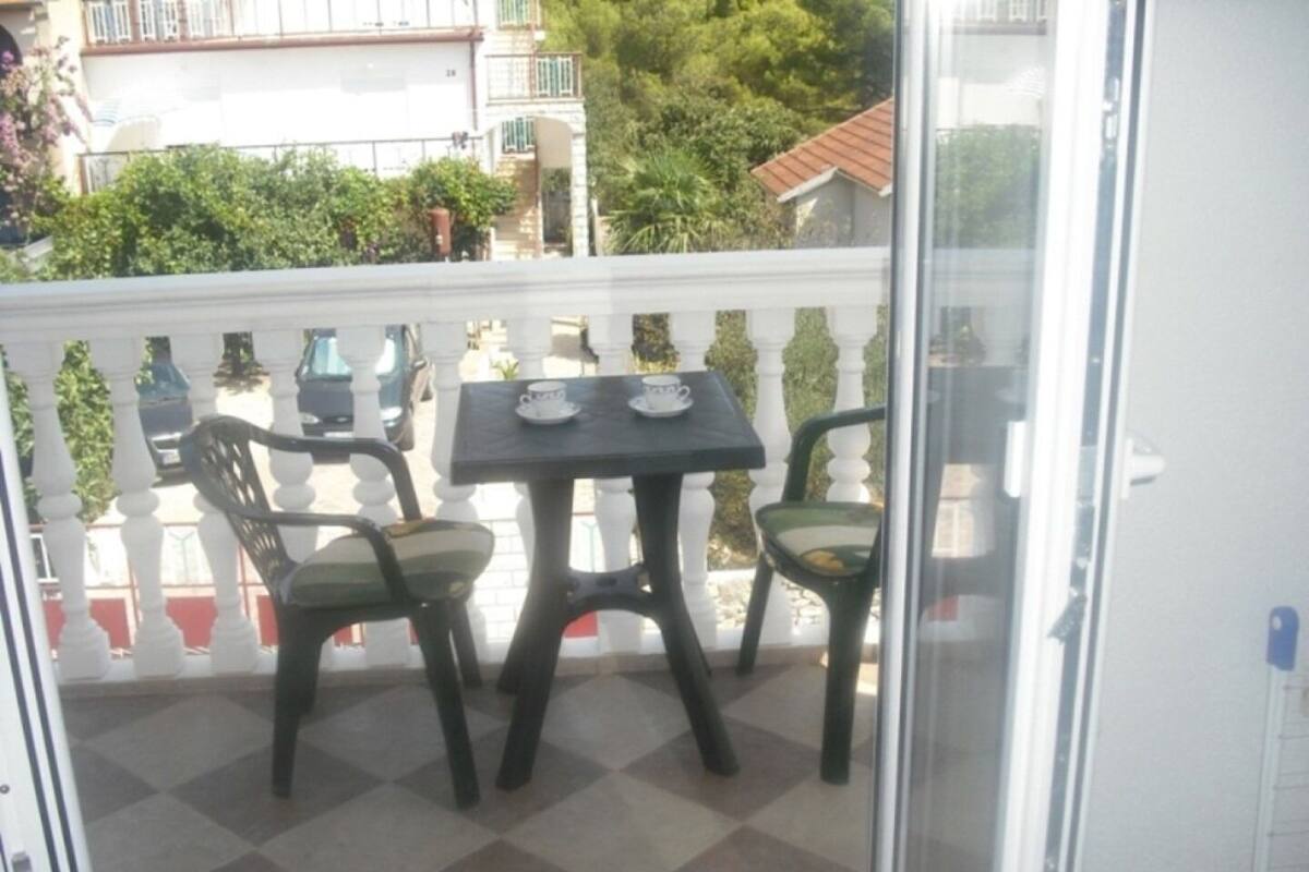 A balcony with a checkered floor, two chairs, and a table with two cups.