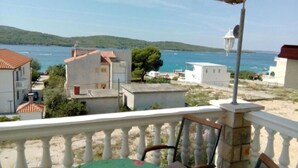 A coastal view from a balcony with a white railing, overlooking a sea with boats, and buildings with red-tiled roofs. - Apartments Maca (Sibenik)