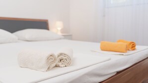 Una cama bien hecha con toallas blancas y amarillas, un cabecero de madera y una mesita de noche con una lámpara.