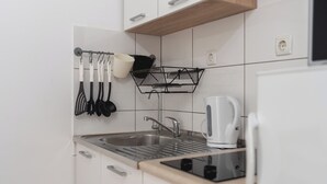 Una cocina moderna con armarios blancos, un lavamanos de acero inoxidable y una tetera en la encimera.