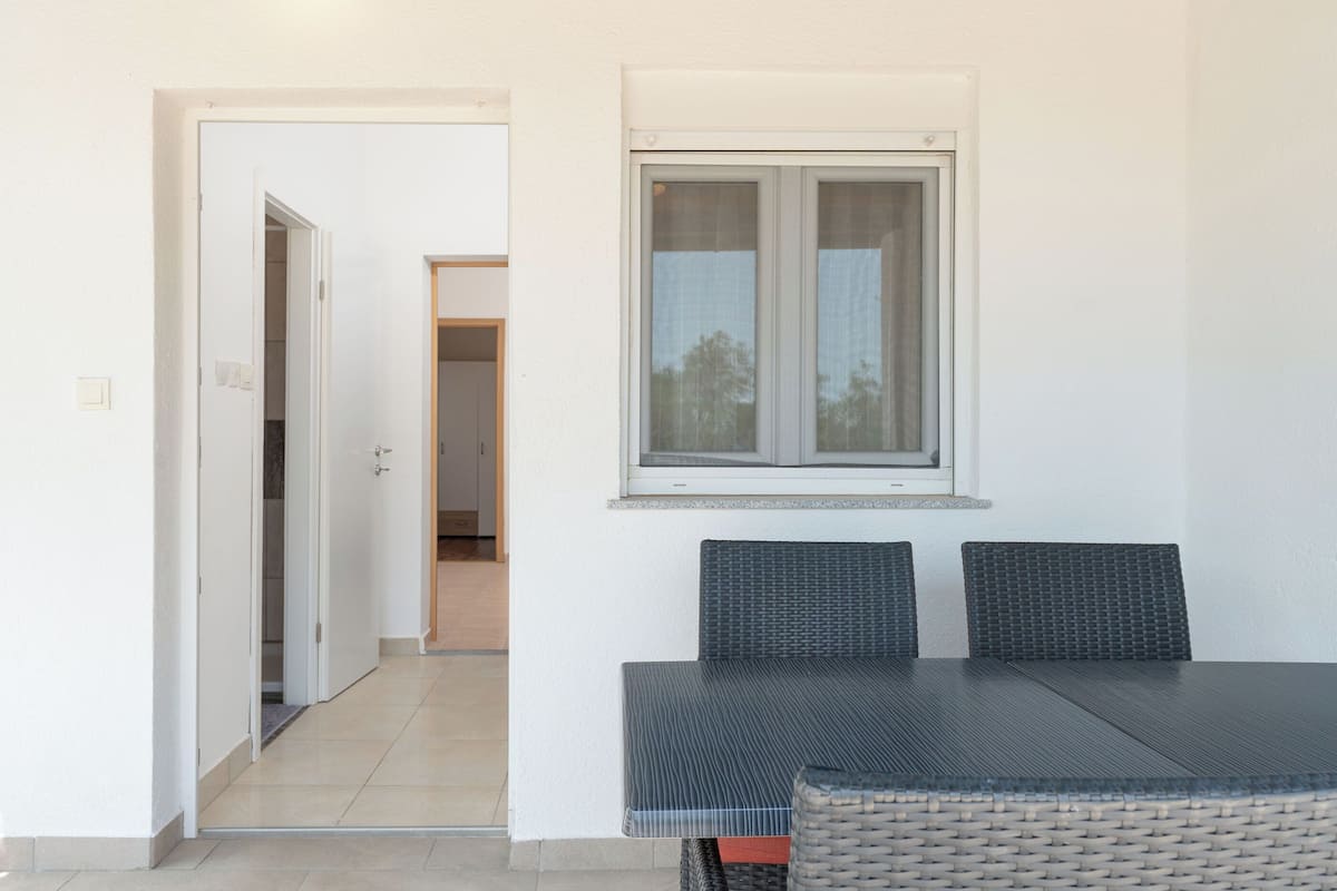 Ein Zimmer mit einem Esstisch und Stühlen, einem Fenster mit Vorhängen und einer Tür zu einem anderen Raum.