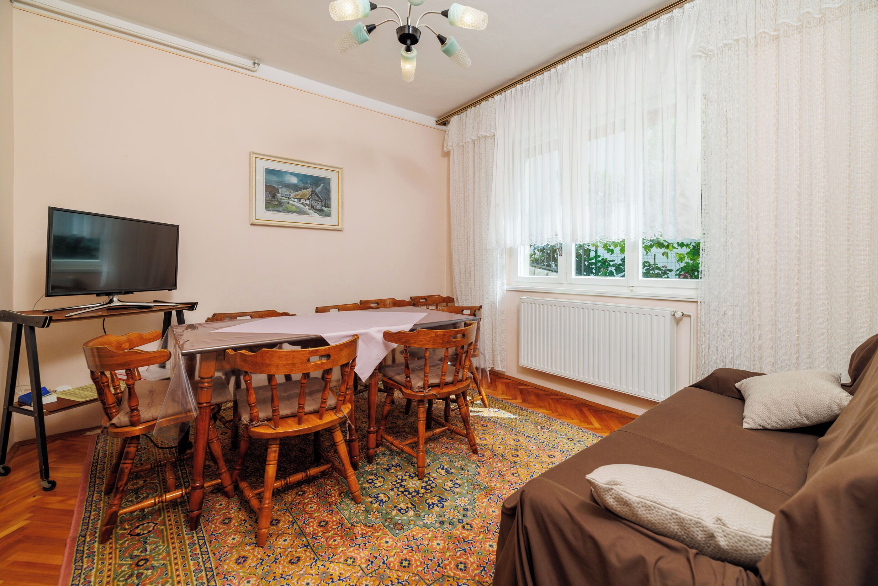 A dining area with a table and chairs, a television, a framed picture on the wall, and a window with curtains.