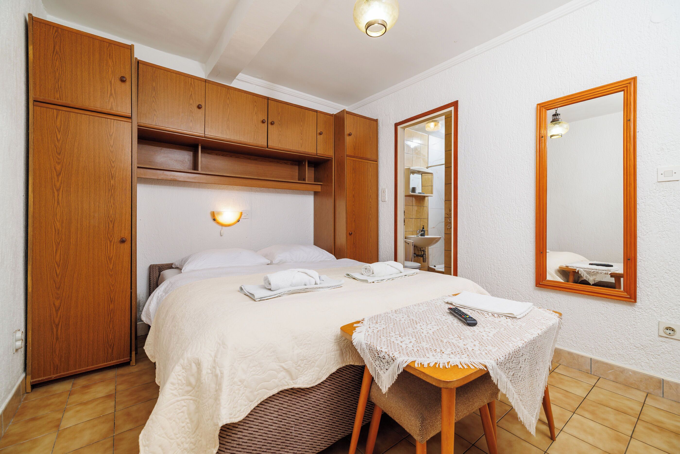 A bedroom with a bed, wooden wardrobe, bedside table, and a mirror.