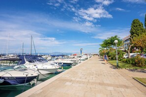 Un puerto deportivo con barcos amarrados, un paseo marítimo pavimentado y un cielo despejado.