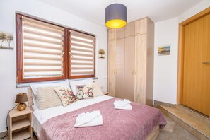 Une chambre à coucher comprenant un lit, une armoire, une table de chevet et une fenêtre avec des stores.