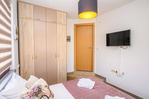 Una habitación de hotel con cama, armario, televisor y puerta que da a un pasillo.