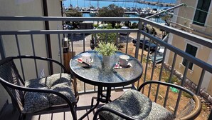 A balcony with two wicker chairs, a small round table with a cup and saucer, and a view of a marina with boats and mountains in the distance. - Apartment Neo (Malinska-Dubasnica)