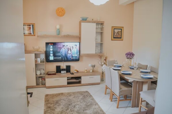A modern living room with a flat-screen TV, wooden entertainment unit, dining table with chairs, and a decorative vase. - House Mili (Zagvozd)