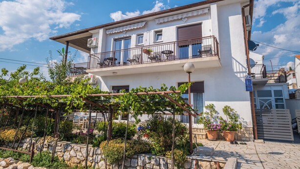 A two-story building with a balcony, outdoor seating, and potted plants. - Rooms Relax (Novi Vinodolski)
