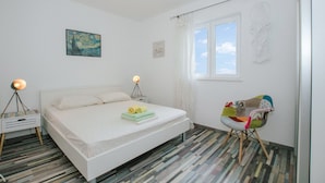 A bedroom with a bed, two bedside lamps, a window, and a chair with a colorful cushion. - Apartment Florio (Trogir)