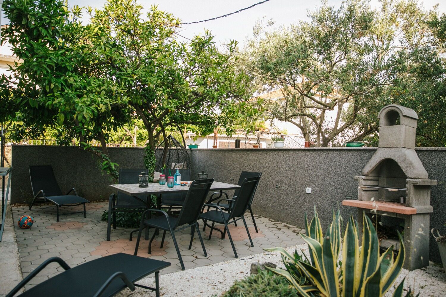 Un patio al aire libre con mesa y sillas, una parrilla de piedra y una pared cubierta de plantas trepadoras.