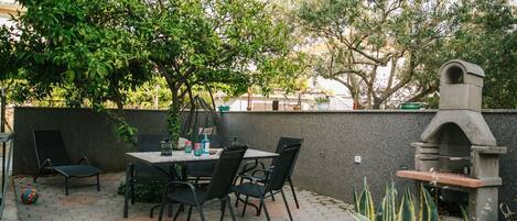 Un patio al aire libre con mesa y sillas, una parrilla de piedra y una pared cubierta de plantas trepadoras.